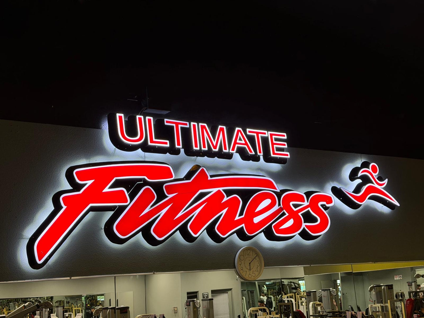 Red and white halo-lit channel letters and running logo inside a fitness center.