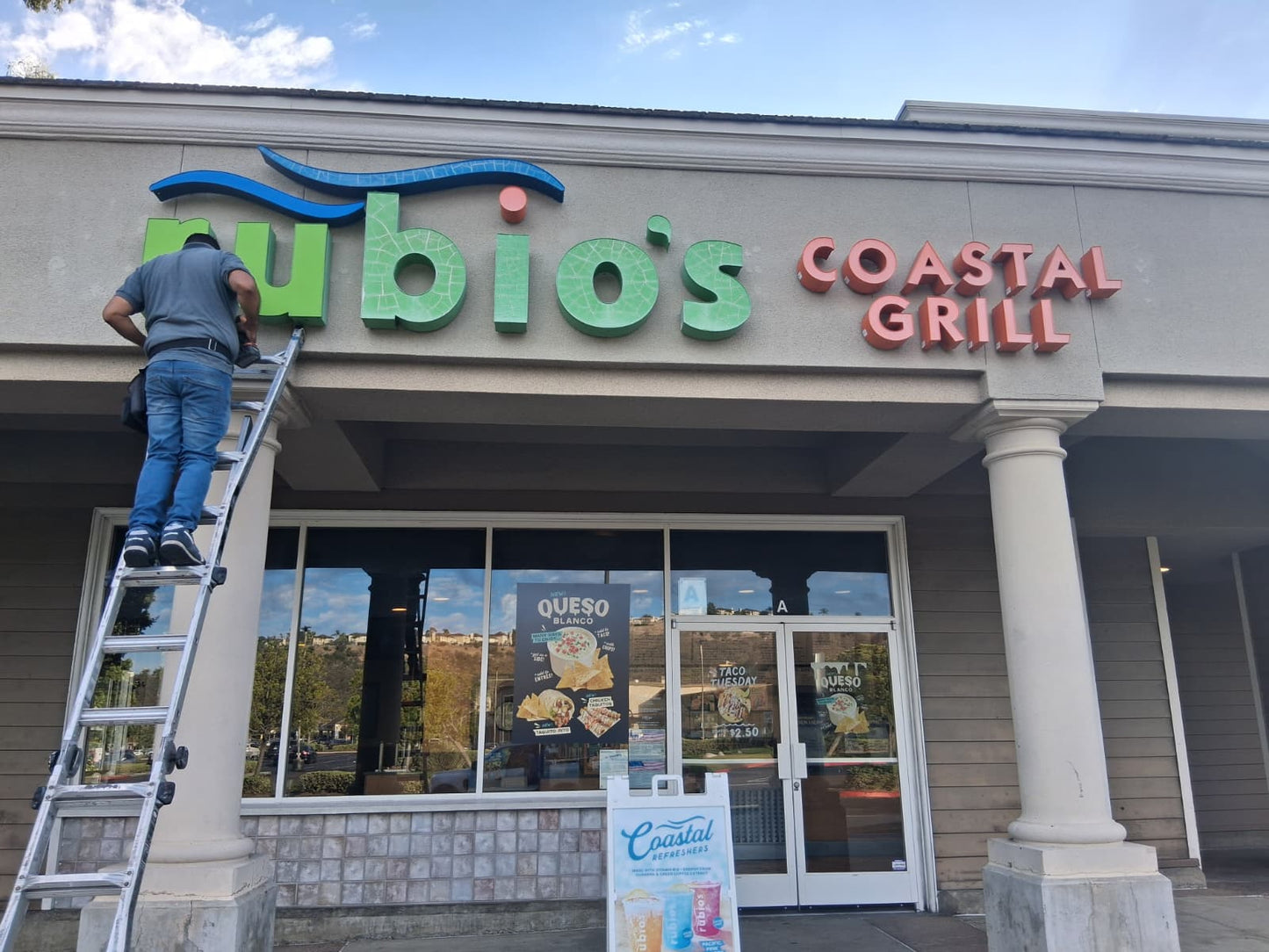 Installer mounting green and red dimensional storefront letters above a restaurant entrance.
