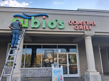 Installer mounting green and red dimensional storefront letters above a restaurant entrance.